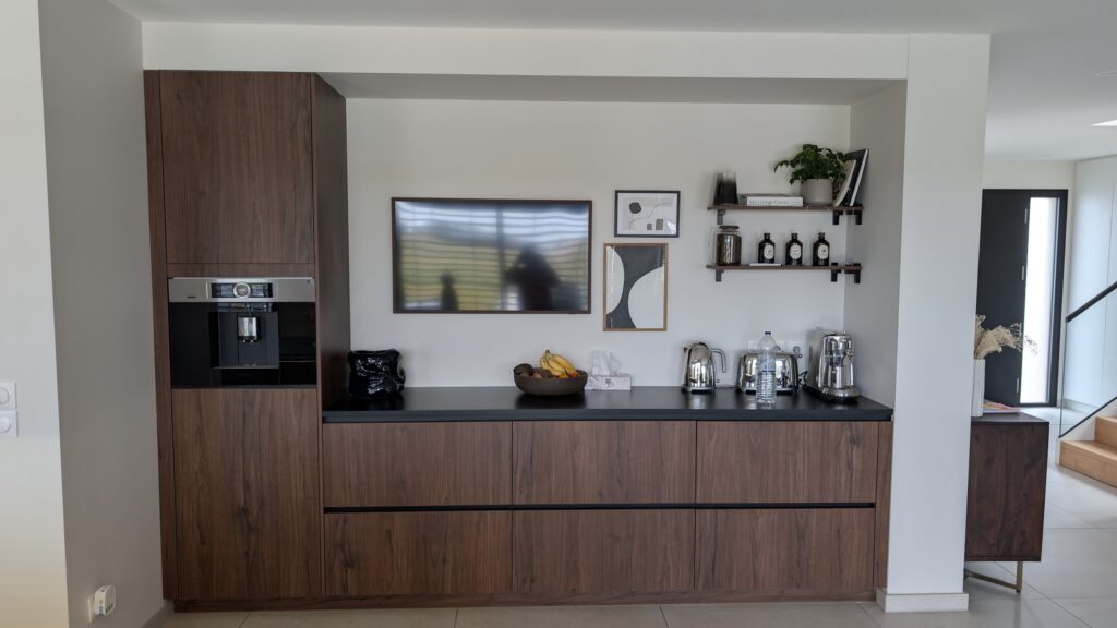 Découvrez cette cuisine HÄCKER réalisée à Évrange, aux portes du Luxembourg : alliance élégante du noyer 1099AV et du blanc polaire 2135VV, plan de travail en céramique LAMINAM Noir Désir, électroménager BOSCH intégré et bâti sur-mesure confectionné par Direct Cuisine.